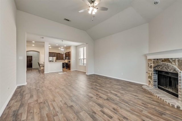 unfurnished living room featuring baseboards, visible vents, a fireplace with raised hearth, wood finished floors, and ceiling fan with notable chandelier