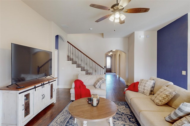 living area featuring arched walkways, ceiling fan, dark wood-type flooring, and stairs