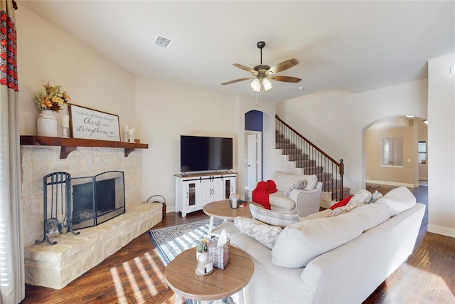 living area with arched walkways, visible vents, a stone fireplace, and wood finished floors