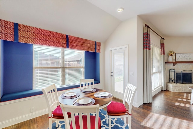 dining area with baseboards, vaulted ceiling, wood finished floors, and a stone fireplace