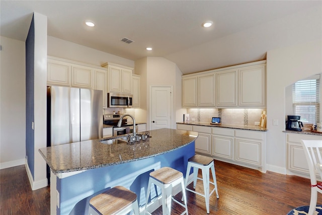 kitchen with dark stone counters, appliances with stainless steel finishes, dark wood-style flooring, and a sink