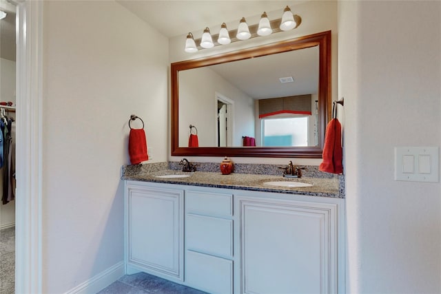 bathroom with a walk in closet, a sink, baseboards, and double vanity