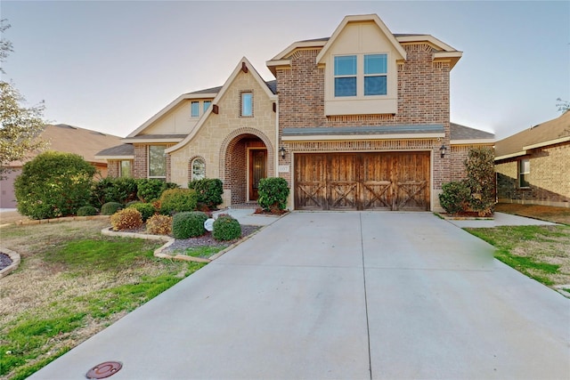 view of front of house featuring an attached garage, stone siding, concrete driveway, and brick siding