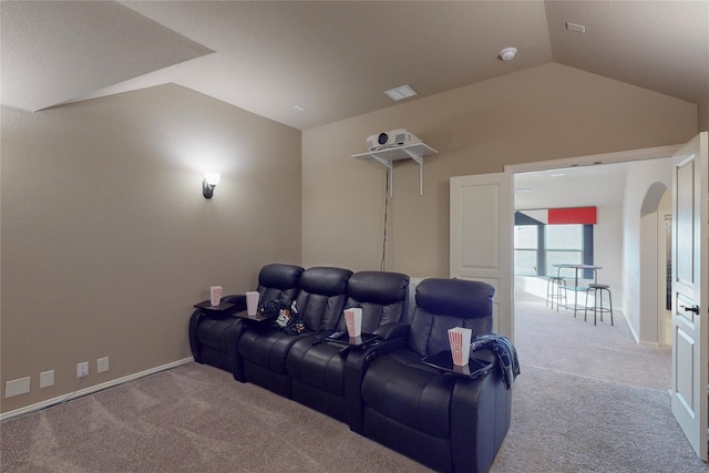 carpeted cinema room featuring lofted ceiling, arched walkways, visible vents, and baseboards