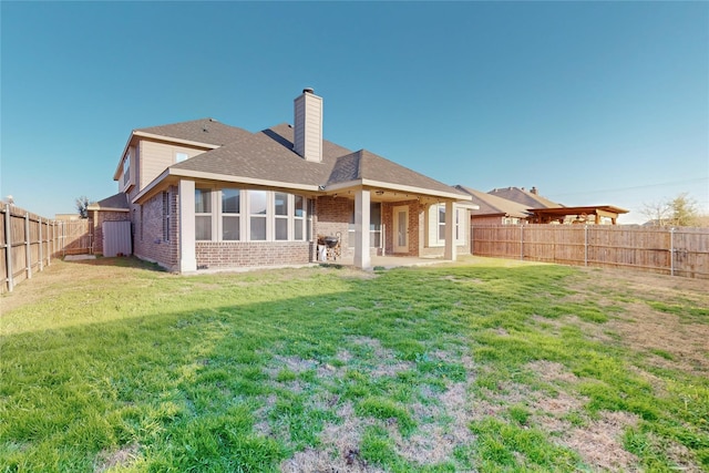 rear view of property featuring brick siding, a chimney, a shingled roof, a lawn, and a fenced backyard