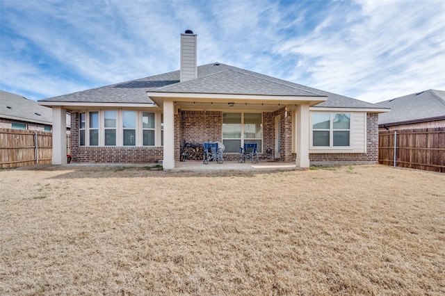 back of house with brick siding, a yard, a chimney, a patio, and a fenced backyard