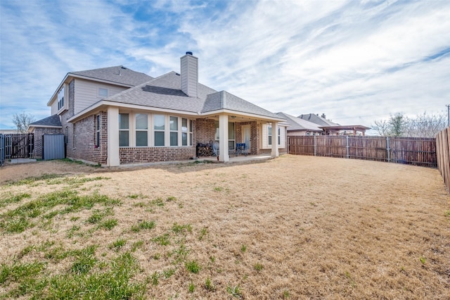 back of property with brick siding, a chimney, a lawn, a patio area, and a fenced backyard