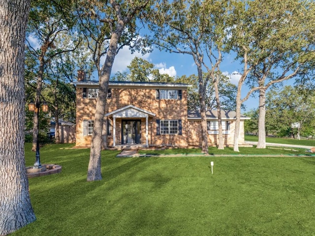 colonial home with a front lawn, a chimney, and brick siding