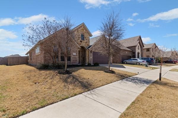 view of front of house with stone siding, fence, concrete driveway, a front yard, and an attached garage