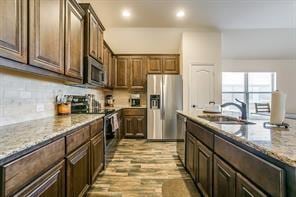 kitchen featuring light stone counters, light wood-style flooring, stainless steel appliances, a sink, and decorative backsplash