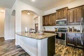 kitchen featuring appliances with stainless steel finishes, dark wood-type flooring, a sink, and light stone countertops