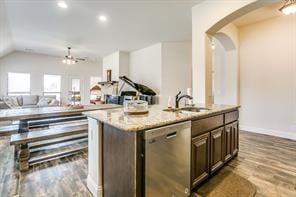 kitchen with dishwasher, an island with sink, light stone counters, open floor plan, and wood finished floors