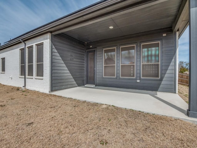 doorway to property featuring a patio, brick siding, and fence