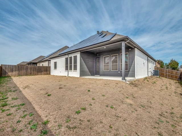 back of house with brick siding, roof mounted solar panels, a patio area, central AC, and a fenced backyard