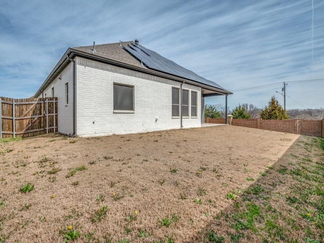 back of property featuring a fenced backyard, solar panels, and brick siding