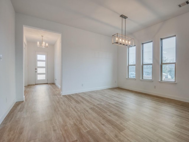 empty room with baseboards, visible vents, light wood finished floors, and an inviting chandelier