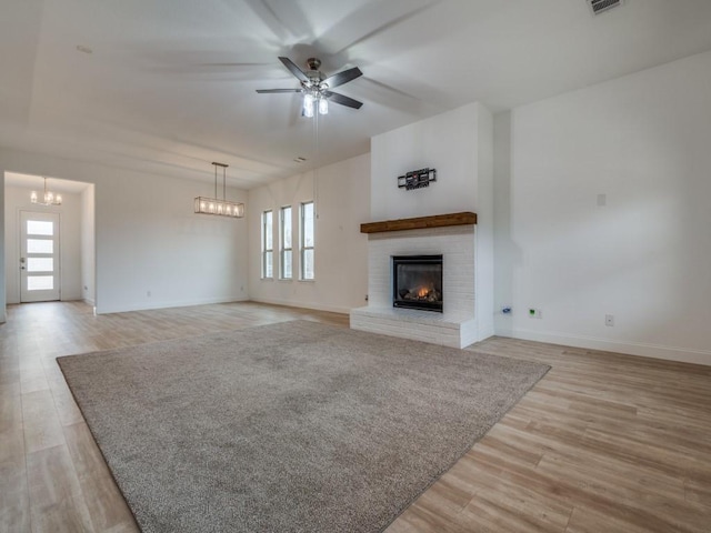 unfurnished living room with light wood-style floors, a brick fireplace, visible vents, and ceiling fan with notable chandelier