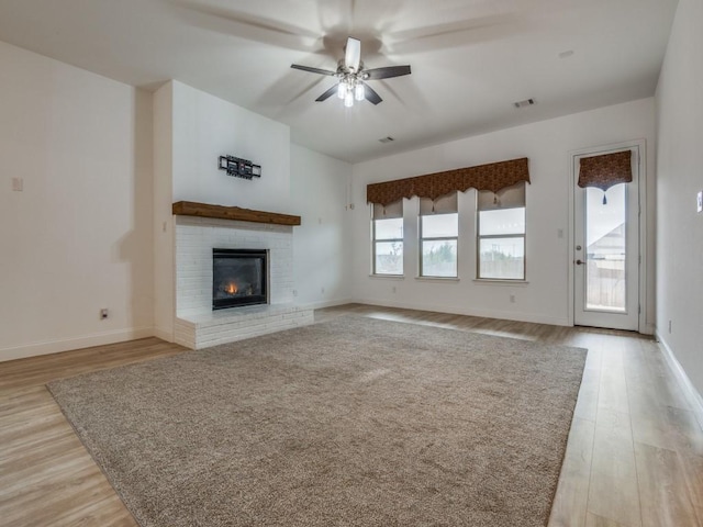 unfurnished living room with light wood-style flooring, a ceiling fan, visible vents, baseboards, and a brick fireplace