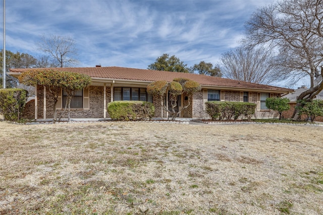 single story home featuring brick siding, a tiled roof, and a front lawn