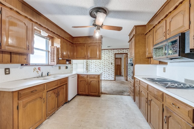 kitchen with appliances with stainless steel finishes, light countertops, a sink, and wallpapered walls