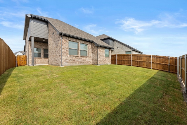 rear view of house with brick siding, a fenced backyard, roof with shingles, and a yard