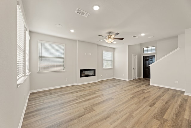 unfurnished living room with light wood-style floors, a glass covered fireplace, visible vents, and baseboards