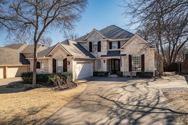 french country home featuring a shingled roof, fence, a garage, stone siding, and driveway