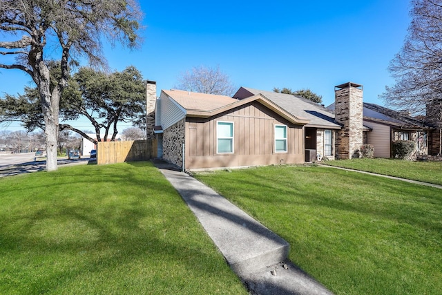 view of front facade with stone siding, a chimney, fence, and a front lawn