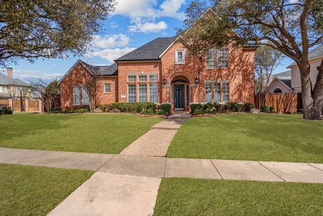 traditional home featuring brick siding, fence, and a front lawn