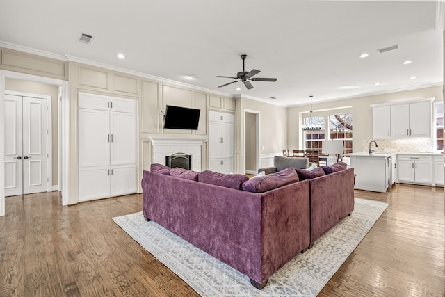 living room with ornamental molding, light wood-type flooring, visible vents, and a fireplace