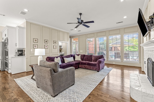 living area with a decorative wall, wood finished floors, visible vents, a brick fireplace, and crown molding