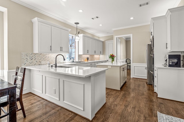 kitchen featuring freestanding refrigerator, visible vents, a sink, and a peninsula