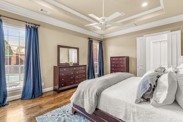 bedroom with ornamental molding, wood finished floors, a raised ceiling, and visible vents