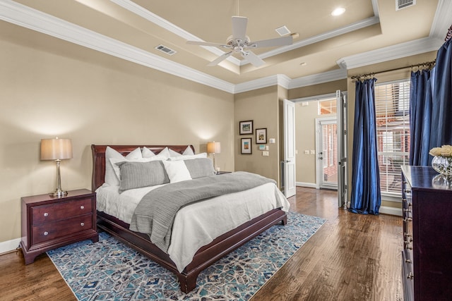 bedroom featuring wood finished floors, visible vents, baseboards, a tray ceiling, and crown molding