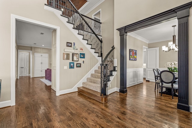 stairs featuring a decorative wall, a notable chandelier, wood finished floors, a towering ceiling, and ornamental molding