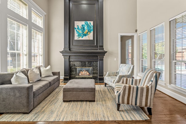 living room with a towering ceiling, wood finished floors, a high end fireplace, and baseboards