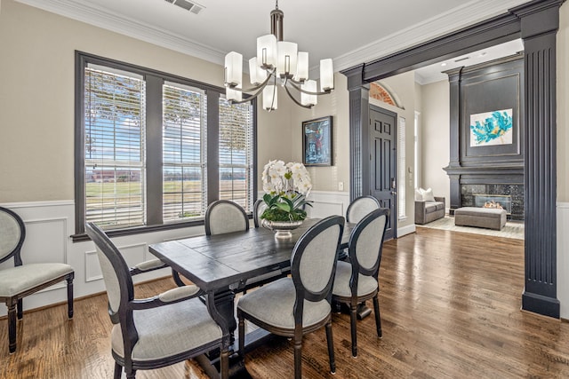 dining room with crown molding, a chandelier, wood finished floors, and wainscoting