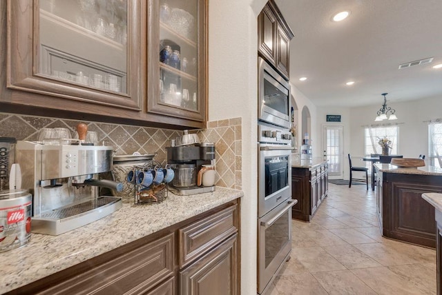 kitchen featuring visible vents, arched walkways, glass insert cabinets, stainless steel microwave, and backsplash