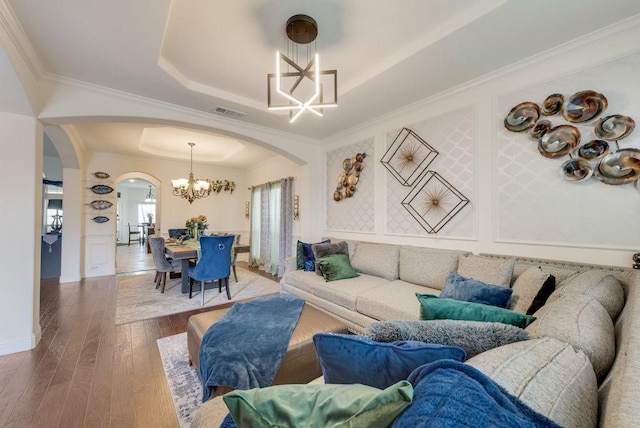 living area featuring arched walkways, a raised ceiling, wood-type flooring, ornamental molding, and a chandelier