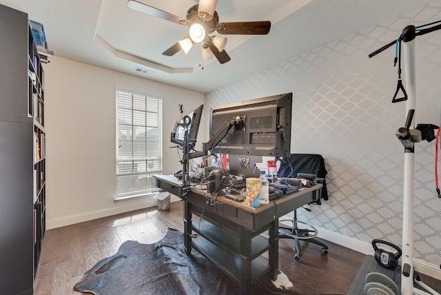 office featuring visible vents, baseboards, ceiling fan, wood-type flooring, and a tray ceiling