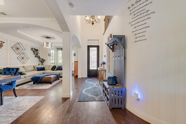 foyer with arched walkways, a notable chandelier, visible vents, baseboards, and dark wood-style floors