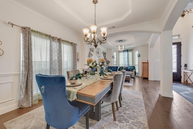 dining area featuring a tray ceiling, crown molding, arched walkways, and wood finished floors