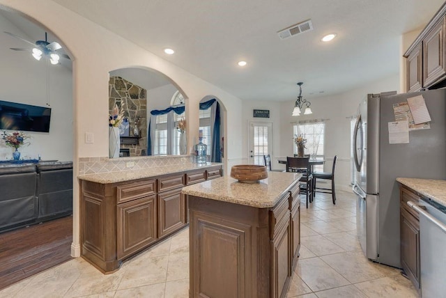 kitchen with visible vents, appliances with stainless steel finishes, a center island, hanging light fixtures, and light stone countertops