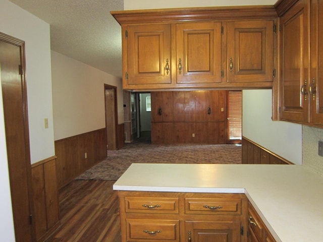 kitchen with brown cabinets, a wainscoted wall, light countertops, wooden walls, and a peninsula