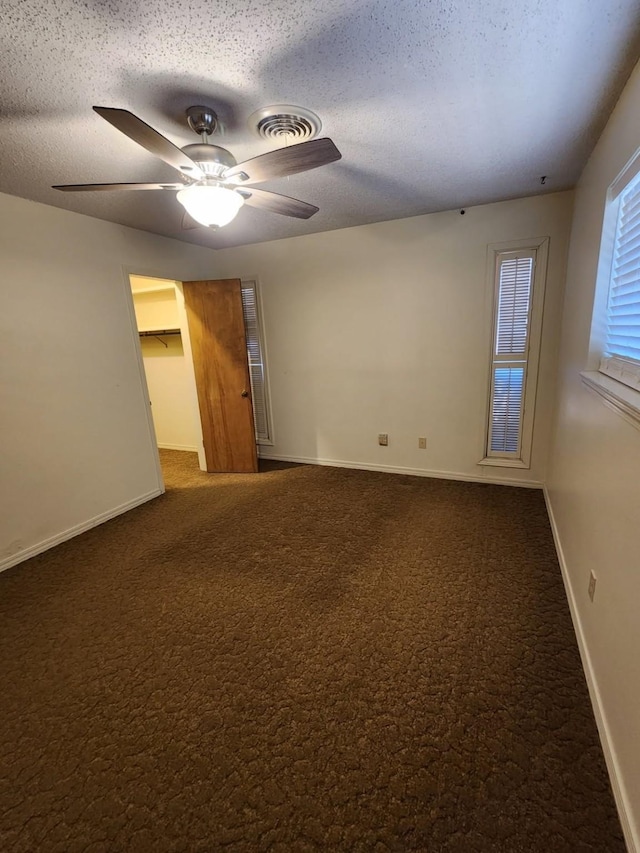 empty room with a textured ceiling, ceiling fan, carpet floors, visible vents, and baseboards