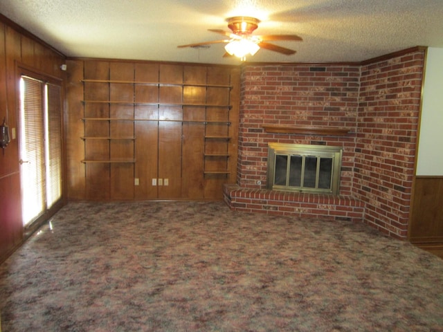 unfurnished living room with a textured ceiling, a brick fireplace, carpet flooring, and wooden walls