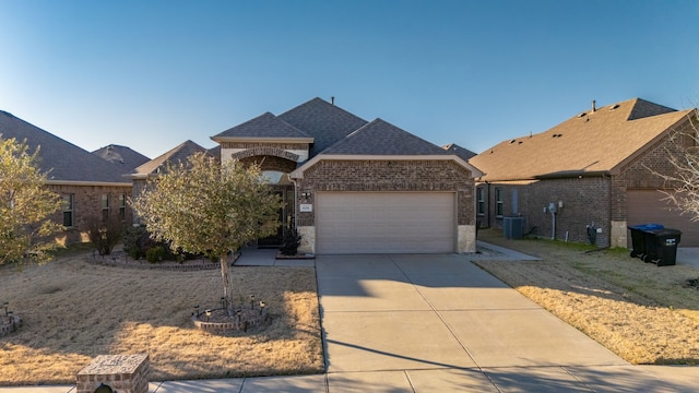 view of front facade with brick siding, a shingled roof, central AC, a garage, and driveway