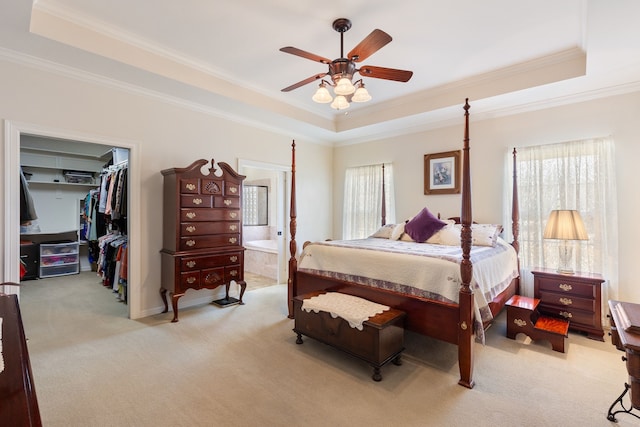 bedroom featuring a walk in closet, a raised ceiling, and light colored carpet