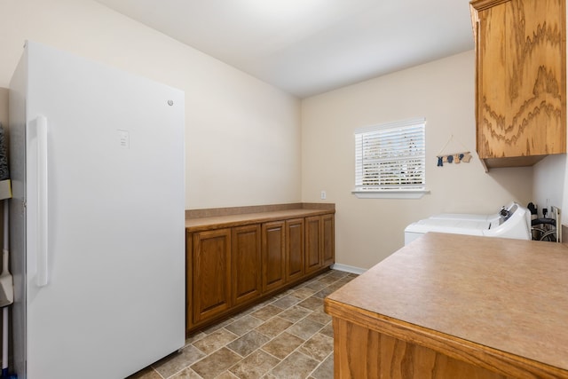 kitchen featuring light countertops, freestanding refrigerator, brown cabinets, stone finish flooring, and washer and clothes dryer