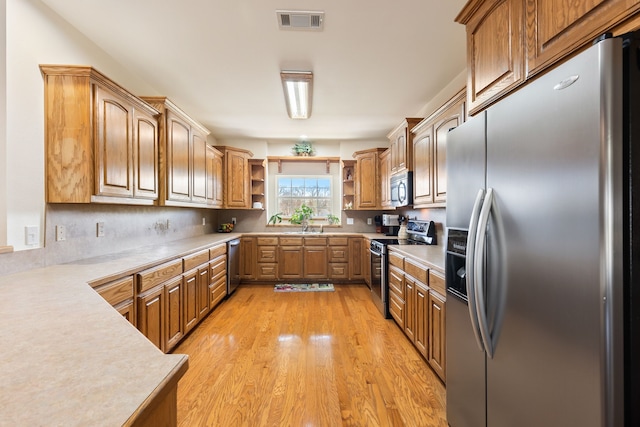 kitchen with light wood finished floors, open shelves, light countertops, visible vents, and appliances with stainless steel finishes